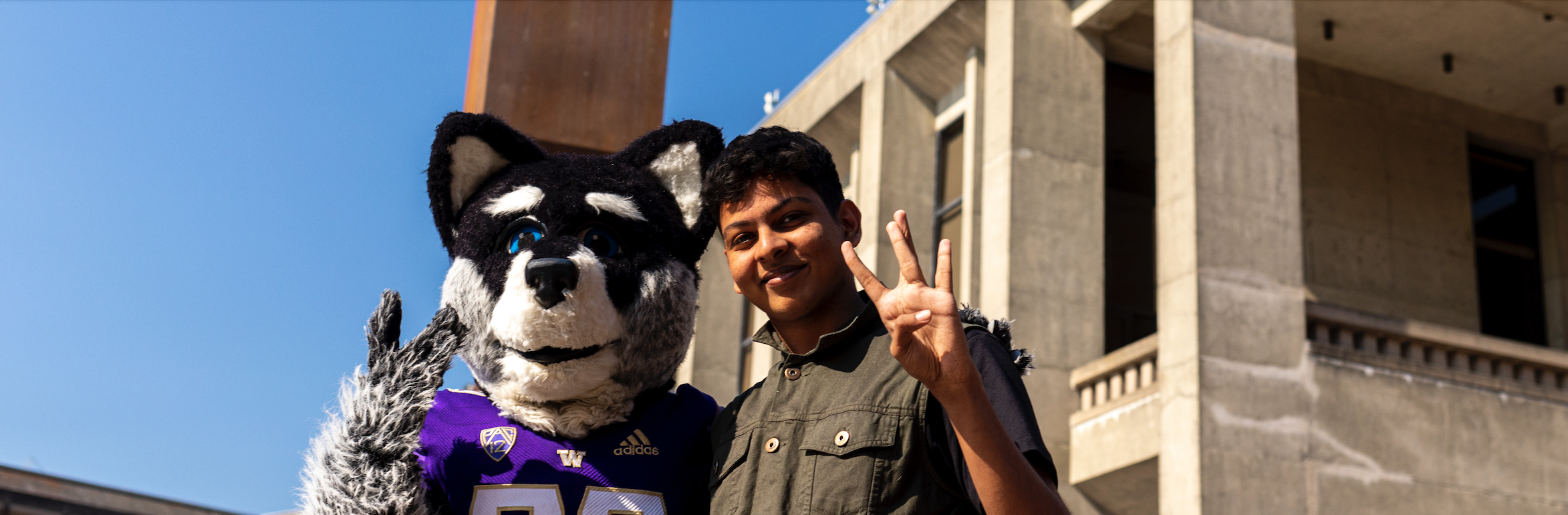 Student throwing up Dubs sign with Harry the Husky.