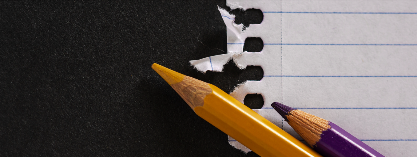 Section of a piece of ruled paper with a yellow and purple pencil laying on top of it.